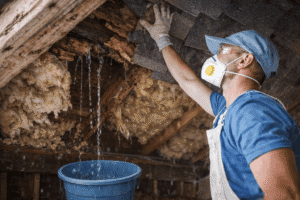 Roofer inspecting severe roof leak damage inside an attic, showing rotted decking, wet insulation, and active water intrusion.